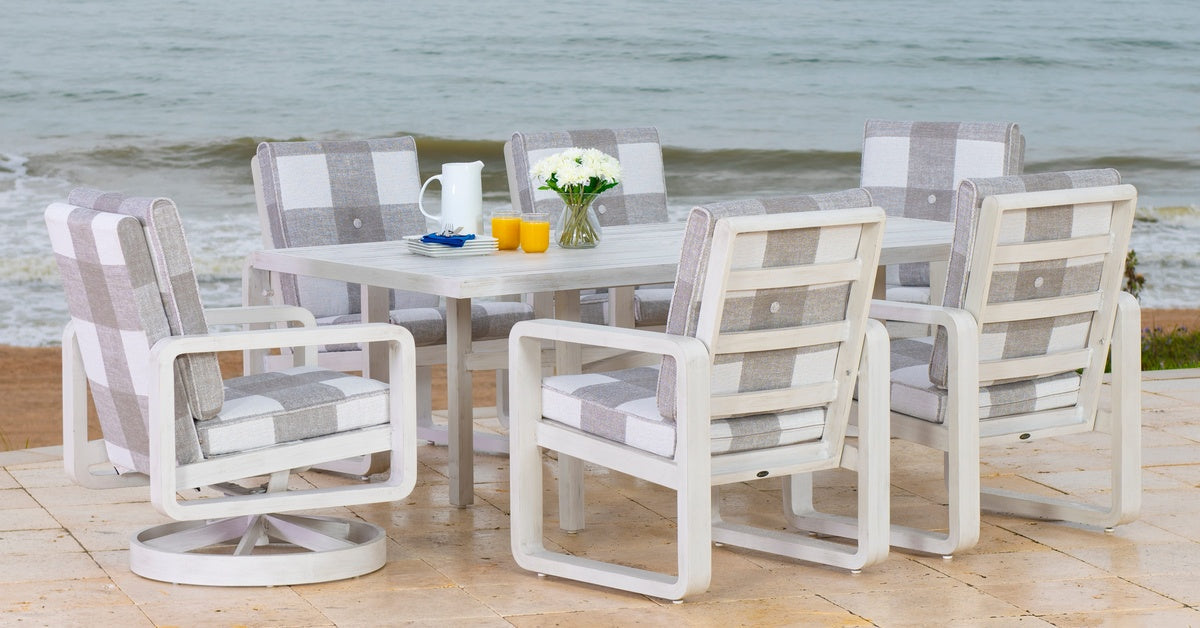 An outdoor dining table set with on a patio near a beach, featuring swivel chairs and plaid cushions.