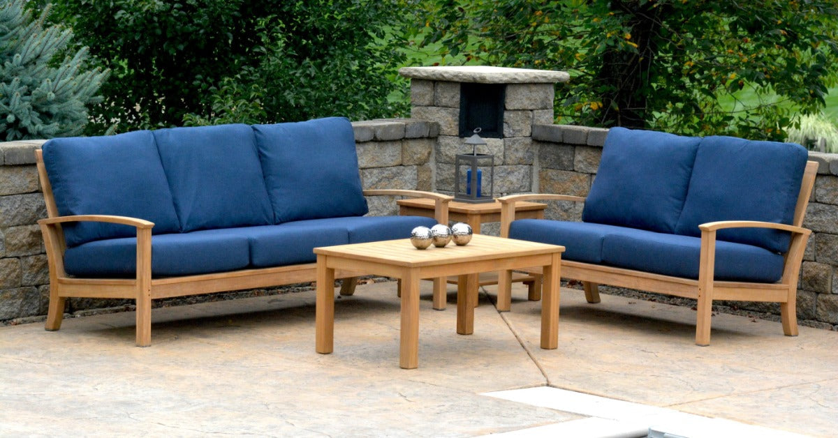 A wooden outdoor furniture set on a pool patio. The set includes a loveseat and a full couch with blue cushions.
