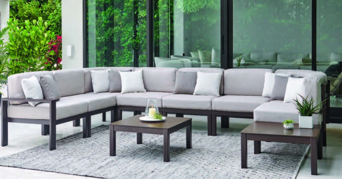 A large, outdoor sectional piece with a dark wooden frame, grey cushions, and a wooden coffee table in the middle.