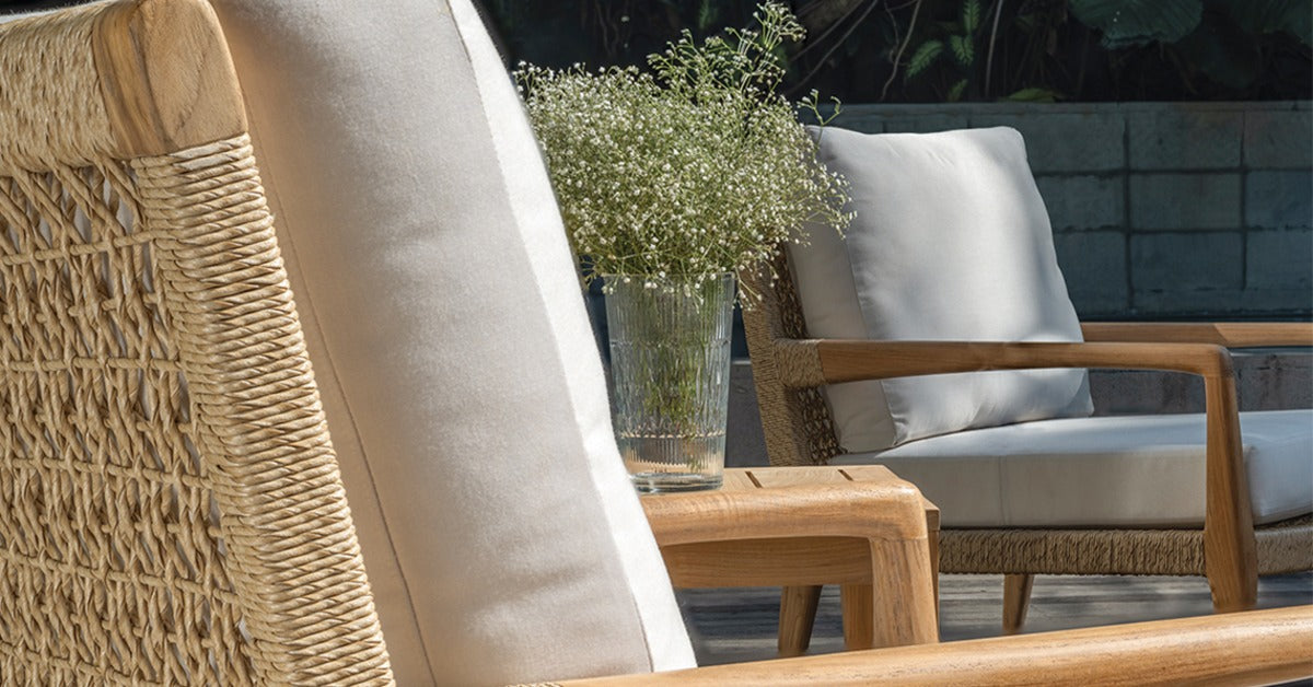 A close-up of the back, cushions, and armrest of an outdoor wicker chair with an end table and another chair next to it.