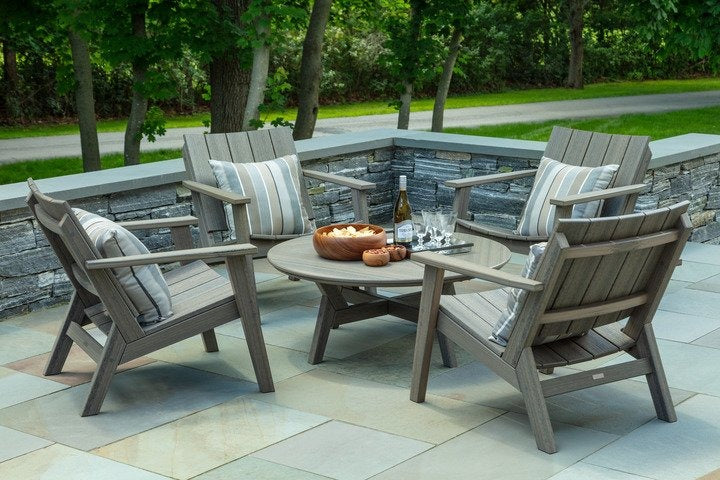 An outdoor furniture set with four chairs with pillows surrounding a round coffee table filled with drinks and snacks.