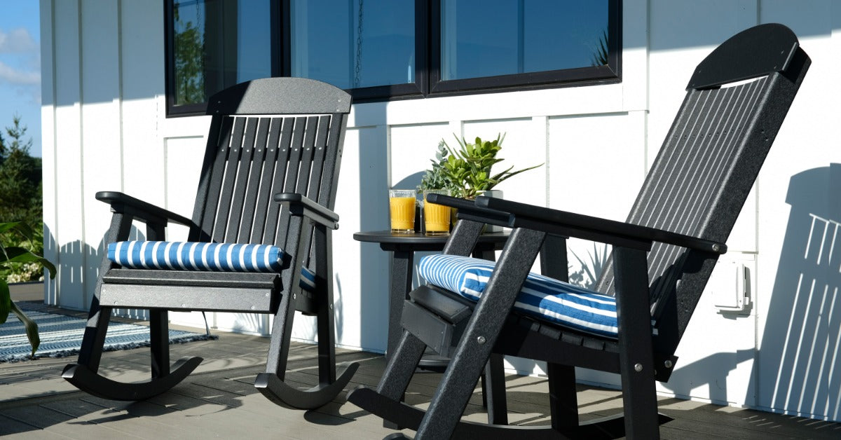 A close-up of two black rocking chairs with blue-and-white cushions with a small endtable between them on a porch.