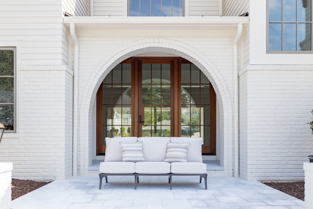 A Hartley sofa with white cushions and striped throw pillows in front of an arched doorway on a stone patio.