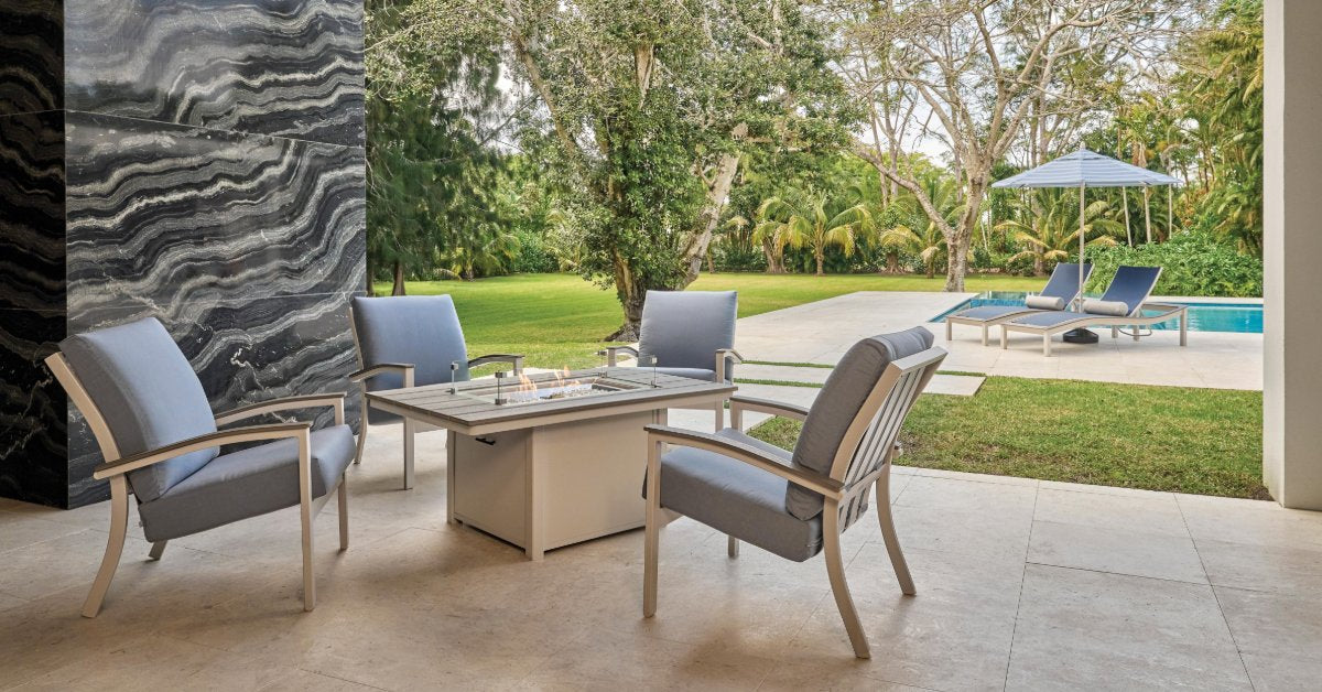 A woven outdoor patio seating set with a cushioned sofa, chairs, and a coffee table arranged on a stone terrace.