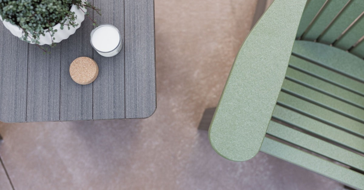 A gray outdoor table beside a green chair, with a potted plant and two small round containers on top.